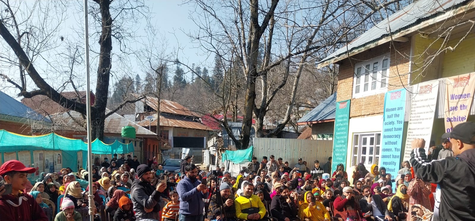 A crowd watching a performance at an outdoor event with campaign banners on the walls