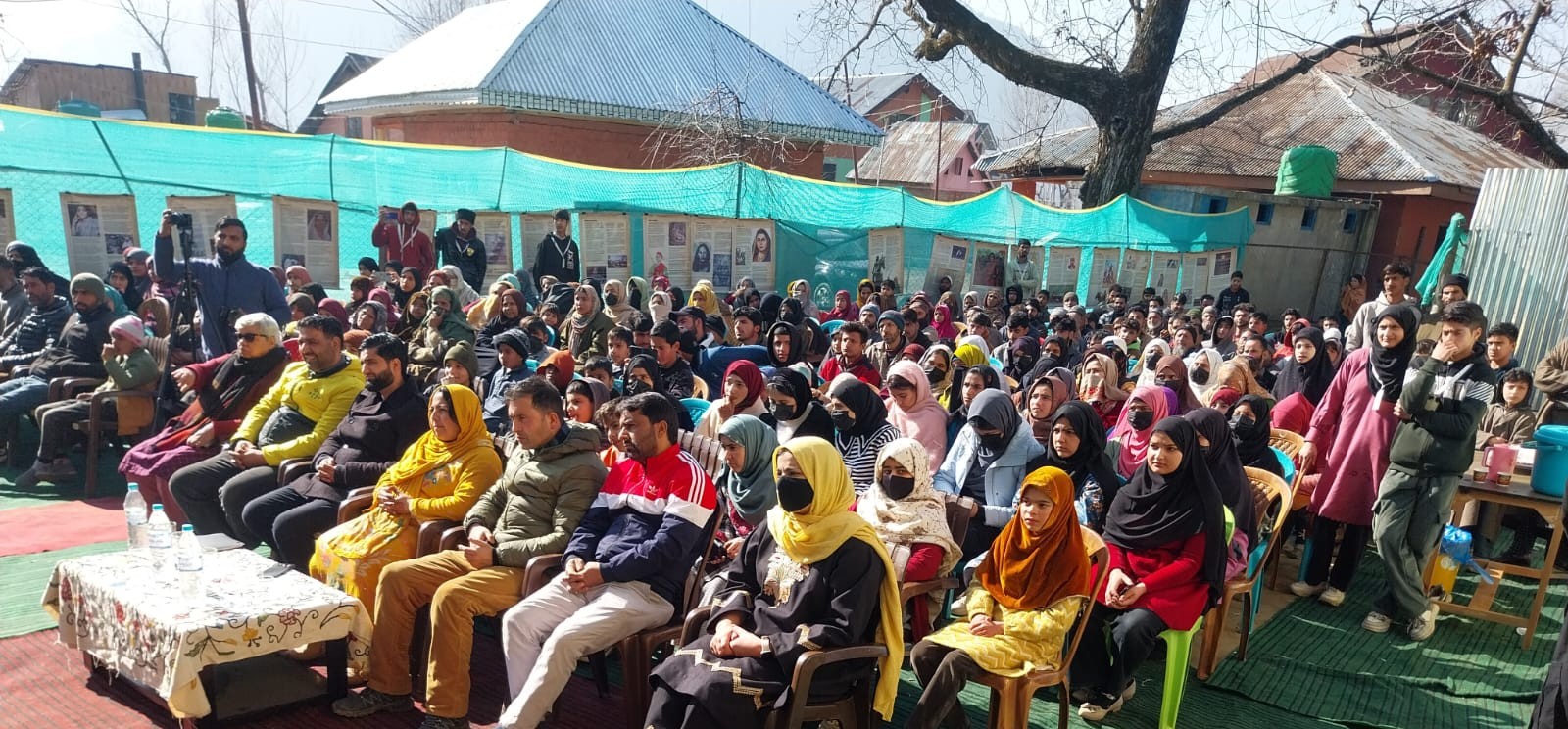 Rows of women and men seated attentively at an outdoor community programme